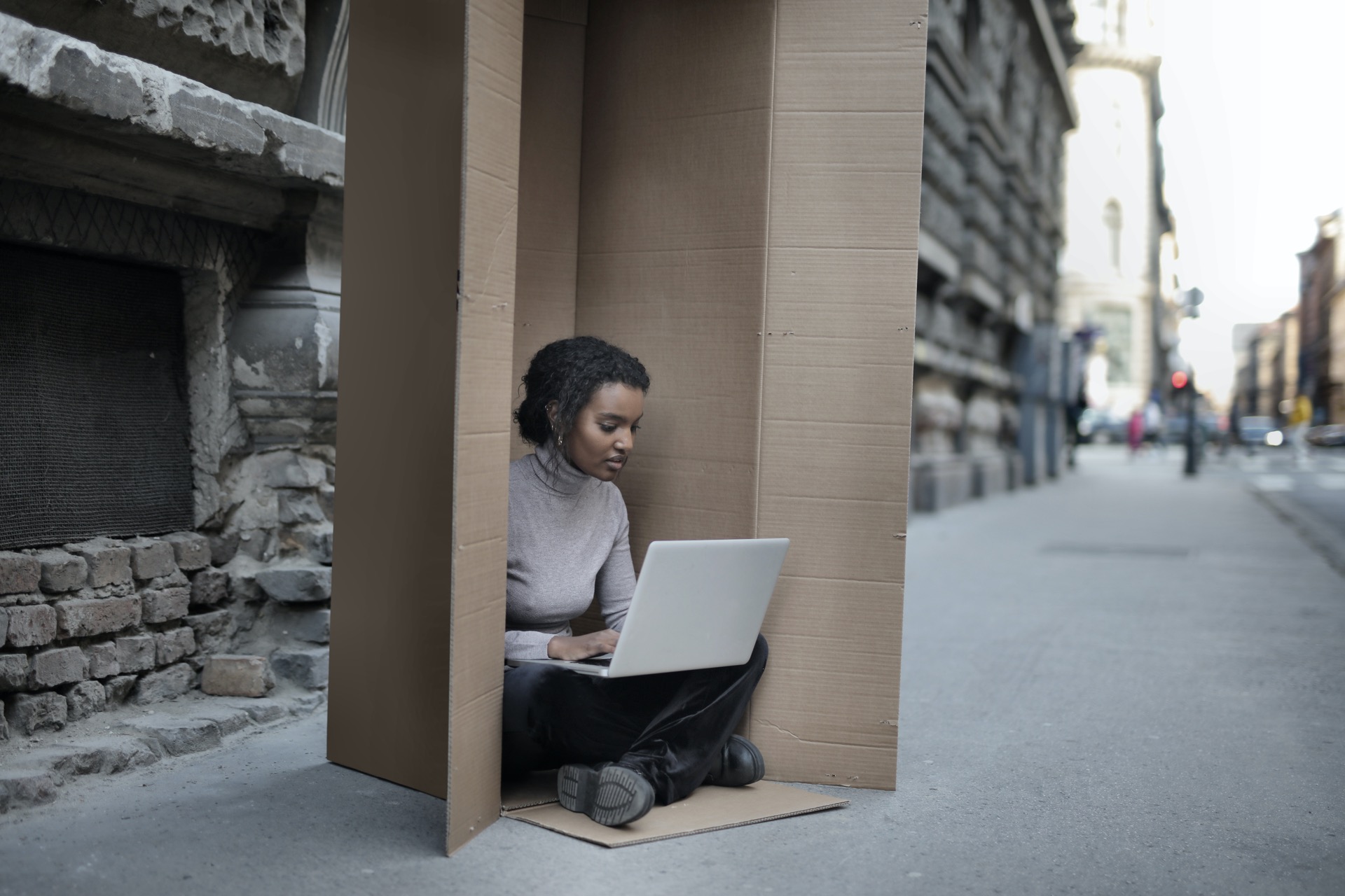 Girl in box with laptop in an alleyway.